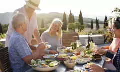 A group of mature friends are sitting around an outdoor dining table in Tuscany, Italy