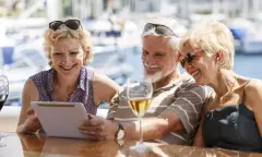 Senior friends smiling and using a digital tablet on a yacht.