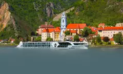 Exterior of the Jane Austen cruise ship passing by buildings with terracotta roofs