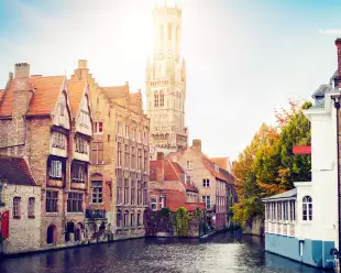 View of the waterfront buildings, canal and bell tower on a sunny day in Bruges, Belgium
